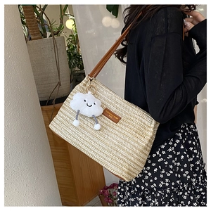 Detail of hand-woven beige straw bucket bag with brown leather strap and cloud charm
