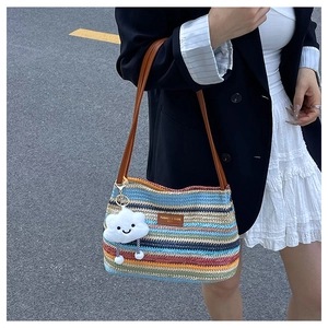 Detail of colorful striped straw tote bag featuring brown leather strap and cloud charm