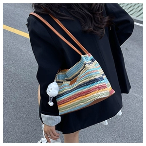 Detail of colorful striped straw tote bag with brown leather straps and plush charm
