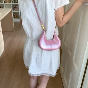 Pink patent leather crescent shoulder bag with gold hardware worn as an underarm bag