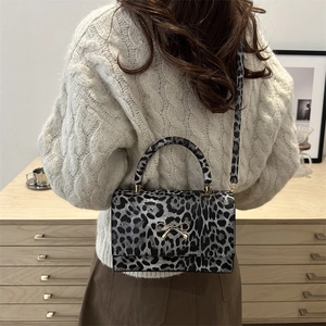 Leopard print crossbody bag with gold bow clasp, shown with model in home setting