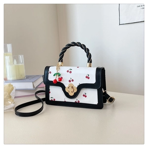 Close-up of cute cherry print handbag with golden floral twist lock and detachable charm