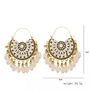 Detailed view of bohemian gold fan earrings with white enamel and drop beads