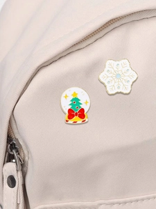 Detailed close-up of Christmas tree and snowflake enamel pins on a canvas backpack