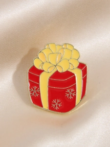 Macro detail of red Christmas gift box enamel pin with yellow bow on champagne satin