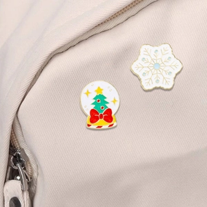 Christmas enamel pins set featuring a green Xmas tree snow globe and white snowflake on a bag
