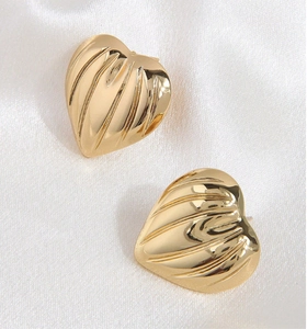 Detailed view of gold heart stud earrings with textured folds on white silk fabric