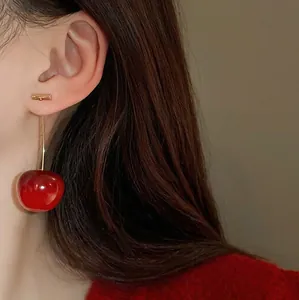 Boucles d'oreilles cerises rouges élégantes avec tiges dorées sur un modèle