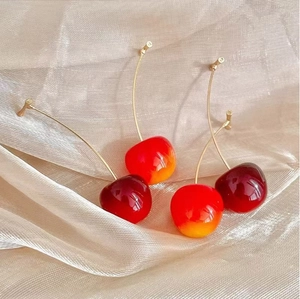 Détail des boucles d'oreilles cerises rouges et oranges sur une soie dorée élégante