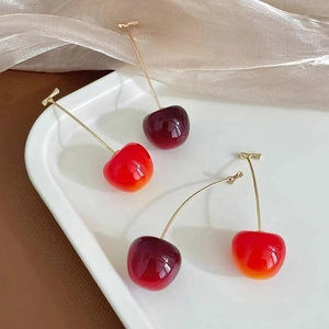 Gros plan de boucles d'oreilles cerises en cristal rouge et bordeaux sur plateau blanc
