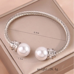 Fashionable silver-colored twisted open bangle with large white pearls and shiny rhinestones