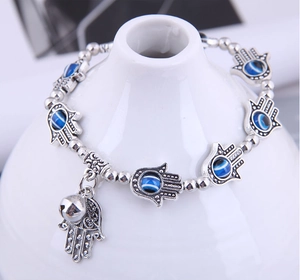Detail of silver beaded bracelet with Hamsa Hand and Evil Eye charms on white ceramic