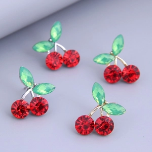Red cherry earrings with green leaf rhinestones set on a blue-grey textured surface
