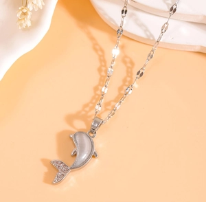 Détail du pendentif dauphin argenté avec pierre œil de chat et zircons sur fond chaud