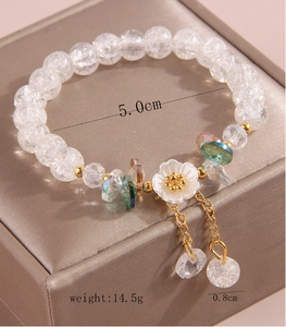 Macro view of white crystal beaded bracelet with floral pendant and golden tassels