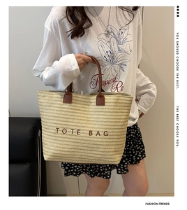 Close-up of woven straw tote bag featuring brown leather handles and embroidered lettering