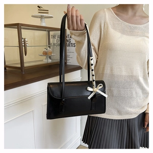 Detail of black leather baguette bag with ribbon bow and checkered strap on a counter