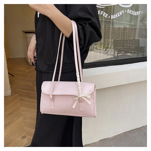 Detail view of pink rectangular shoulder bag with a white ribbon bow on a model
