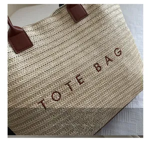 Detail of embroidered TOTE BAG letters and fine straw woven texture with leather handle