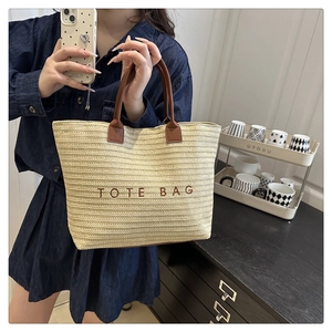 Detail of a large straw tote bag with brown TOTE BAG embroidery and leather handles