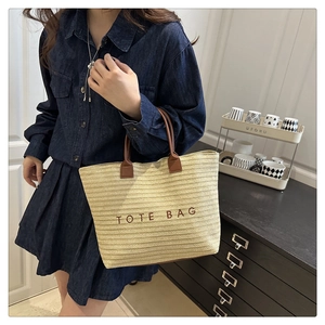Detail of embroidered tote bag lettering with brown leather handles on straw material