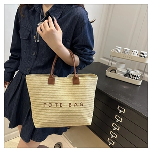 Detail of hand-woven straw tote bag with brown leather handles and TOTE BAG embroidery