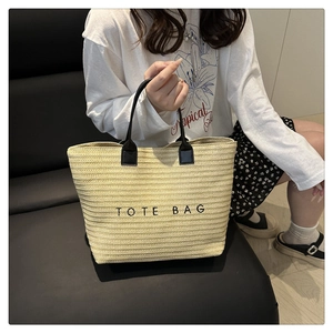 Detail of a large straw tote bag with black leather handles and TOTE BAG lettering