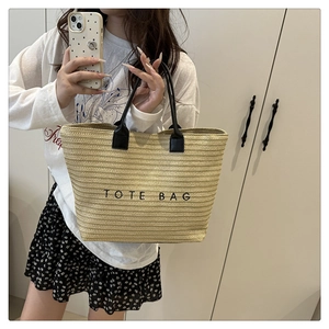 Macro view of woven straw tote bag with black TOTE BAG embroidery and leather handles