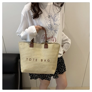 Detail view of woven straw tote bag with brown handles and embroidered TOTE BAG text
