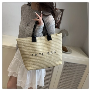 Close-up of beige straw tote bag with black leather handles and embroidered logo