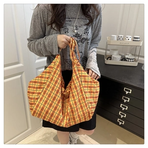 Détail d'un grand sac cabas en toile à carreaux jaunes et rouges porté par un mannequin