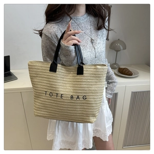 Detail of beige straw tote bag with black handles and TOTE BAG embroidery text
