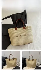 Close-up of woven straw tote bag featuring brown leather handles and TOTE BAG embroidery