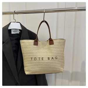 Detail of woven straw tote bag with brown leather handles and embroidered logo lettering