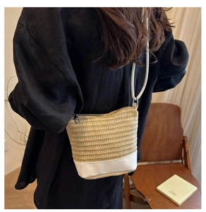 Detail of hand-woven straw bucket bag with white leather base and thin strap on a model