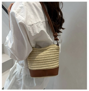 Detailed side view of woven bucket bag with brown leather base and knot strap detail