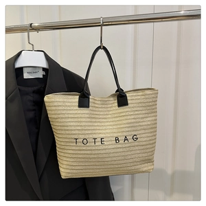Detail view of woven straw tote bag texture and black leather handle on metal hanger