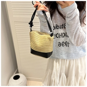 Detail of straw bucket bag featuring black leather base and thick knotted shoulder strap