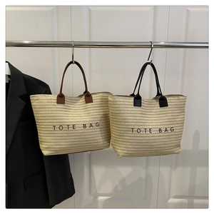 Detail of woven straw tote bags with leather handles and embroidered lettering