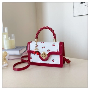Close-up of a red cherry print crossbody bag with woven handle and gold clover lock