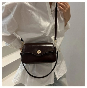 Detail of a dark brown glossy leather crossbody bag with a gold metal twist lock