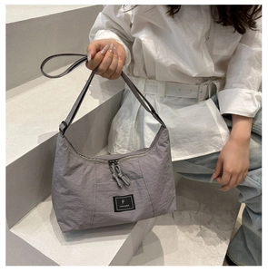 Close-up of grey-purple nylon shoulder bag featuring double zippers and black logo label