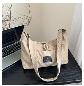 Detail shot of beige nylon tote bag with brand logo on a desk with a laptop