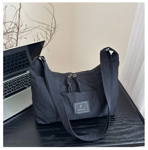 Detail of black nylon shoulder bag featuring dual zippers and branded logo patch