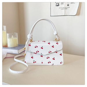 Detailed view of white leather shoulder bag with red cherry prints and golden hardware
