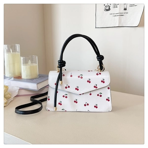 Detail of a chic cream-colored cherry print crossbody bag with black top handle and strap