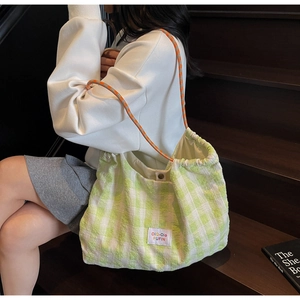 Detail of green checkered tote bag with orange braided rope handle on wooden stairs