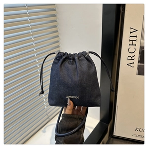Détail du sac seau en denim bleu avec cordon de serrage, logo argenté et haut plissé