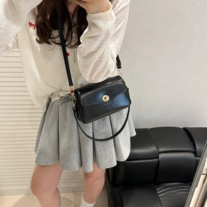 Glossy black patent leather crossbody bag with golden clasp shown on shoulder