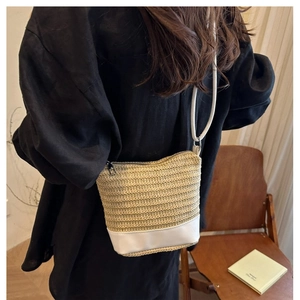 Straw woven bucket bag with white leather base worn by a model in a casual setting